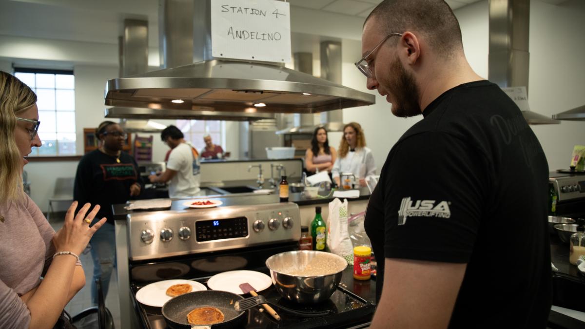 Two students in a large kitchen cooking on a stovetop