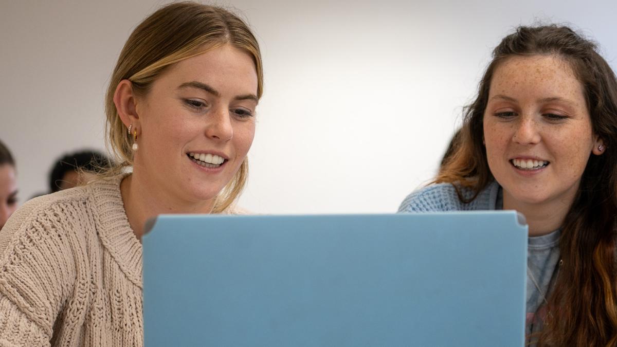 two girls smiling at a laptop