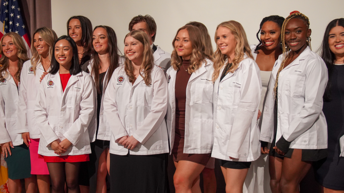 2024 Dietetic Interns lined up on stage in white coats