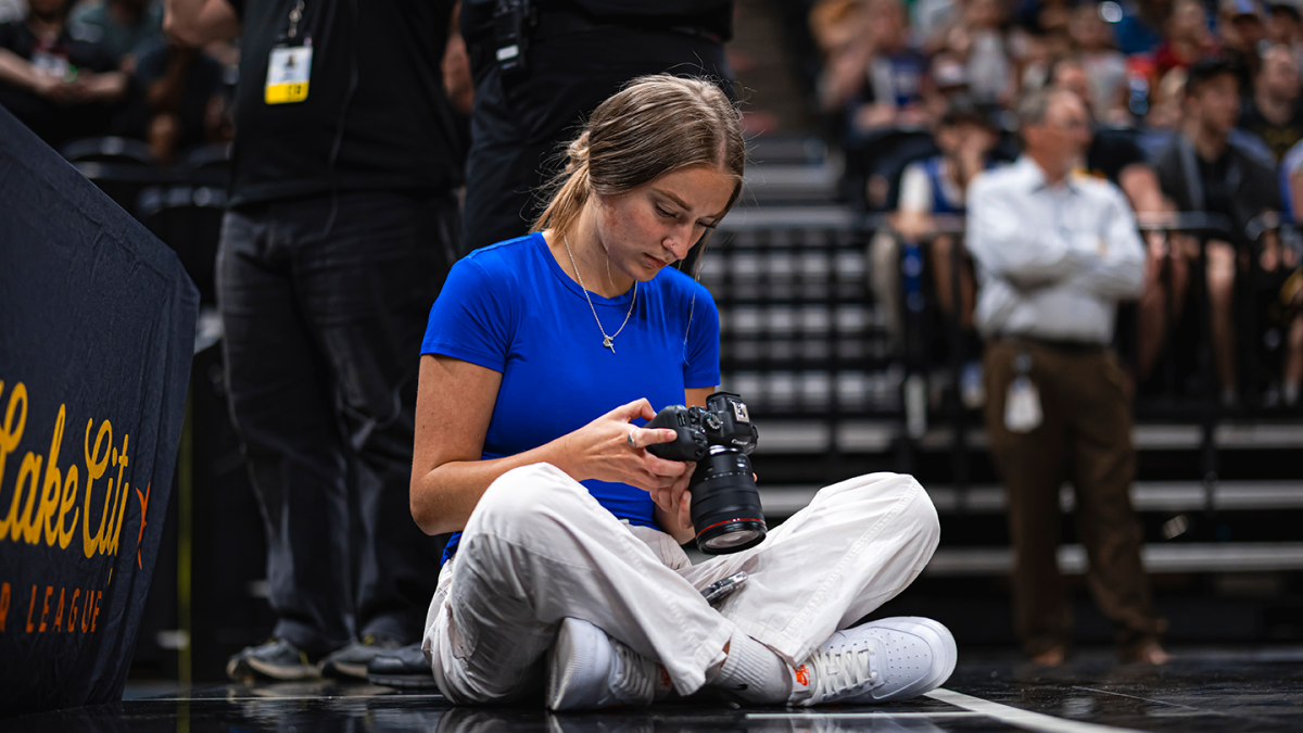 Brooke Brennan sitting sideline on a basketball court with a photography camera
