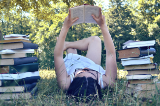 Teen reading in the grass next to stacks of books