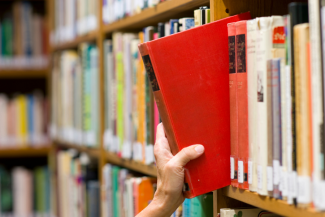 Person pulling a red book off a shelf